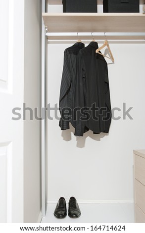 Still life of a professional hotel room wardrobe with a business man tidy black shirts hanging from wooden hangers and masculine shoes. Home interior detail with no people.
