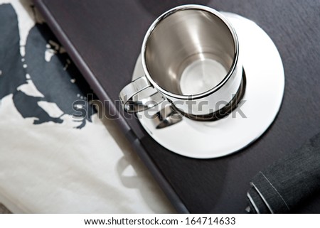 Over head close up still life view of an elegant wooden tray in a hotel restaurant with a shining exclusive silver coffee cup and serviette. Home interior room with no people.