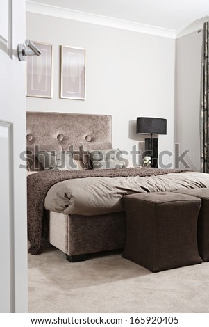 General view of an elegant designer bedroom in a hotel or house through an open door, decorated with brown colors and natural details, home interior with no people.