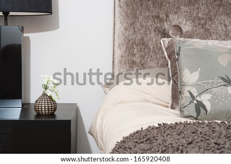 Close up detail view of a bed head in an elegant hotel bedroom with a lamp and side table, cushions and pillows. Home interior with no people.