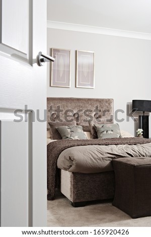 General view of an elegant designer bedroom in a hotel or house through an open door, decorated with brown colors and natural details, home interior with no people.