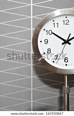 Close up detail view of a metallic silver standing clock against a graphic lines gray wallpaper in a masculine design home, interior.