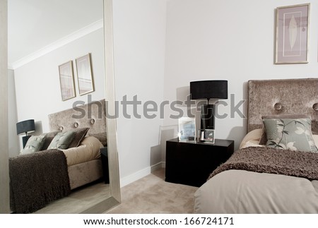 Still life view of an elegant and stylish hotel bedroom decorated in dark brown colors with a large mirror and the reflection of the space. Home interior with no people.