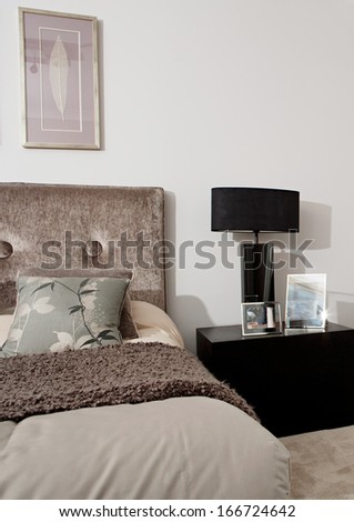 Still Life View Of An Elegant And Stylish Hotel Bedroom Decorated In Dark Brown Colors With A Lamp And Picture Frames On The Bed Side Table. Home Interior With No People.