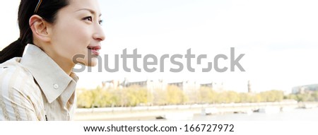 Panoramic close up profile portrait of an attractive and successful Japanese business woman looking ahead and feeling hopeful against a blue sky in a large city during a sunny day.