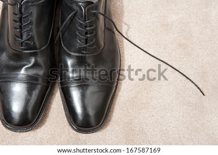 Over head still life detail of the tips of a pair of quality black leather business man shoes resting together on a luxury carpet with laces undone and space around them. Interior view with no people.
