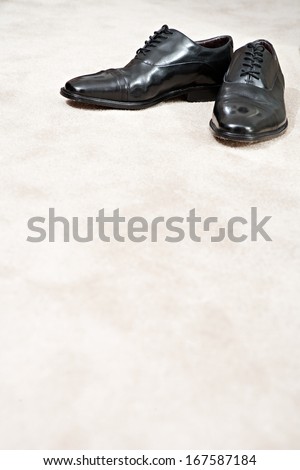 Still life detail of a pair of quality black leather business man shoes on a luxury home carpet with space around them. Interior view with no people.