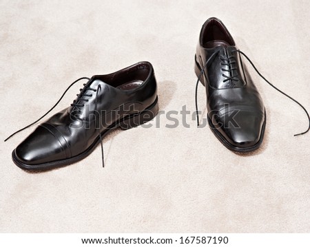 Still life detail of a pair of quality black leather business man shoes resting together on a luxury home carpet with space around them. Interior view with no people.