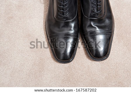Over head still life detail view of the tips of a pair of quality black leather business man shoes resting together on a luxury carpet with space around them. Interior view with no people.