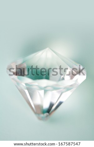 Close up still life detail view of a prism cut gem diamond jewelry piece against a turquoise blue background with light filtering through the glass. Luxury and quality crystal, interior.