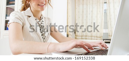 Panoramic close up detail of a professional business woman body section using a laptop computer at her working desk, typing while sitting at her white home office. Office interior.