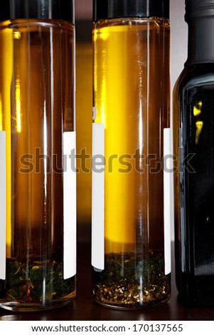 Close up still life detail of glass bottles of healthy and flavored olive oil in a kitchen shelf with the sun lighting the golden color of the oil. Home interior with food and cooking ingredients.