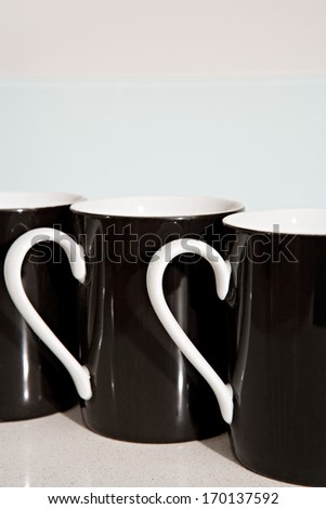 Still life side view of three black and white tea mugs aligned together on a kitchen counter. Home interior coffee drinking detail.