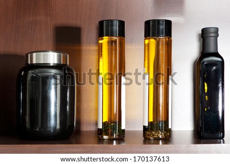 Still life detail view of a wooden kitchen shelf with transparent glass olive oil containers with spices and condiments. Glass bottles of healthy olive oils aligned on a home cupboard. Interior.