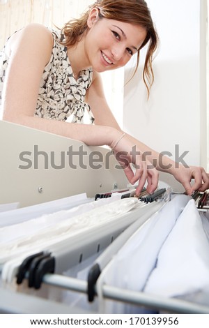 Side portrait view of an attractive office businesswoman flicking through the clients files in an open filing cabinet, searching for and picking a file in an office interior and smiling at camera.