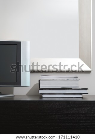Still life view of a high technology bedroom with a flat screen tv and a pile of hard cover books on a wooden cabinet in a luxury home. Elegant hotel room interior with technology.