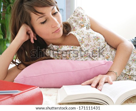 Portrait view of an attractive young college student woman working at home, studying in her bedroom with her college books, laying down at home. Interior.