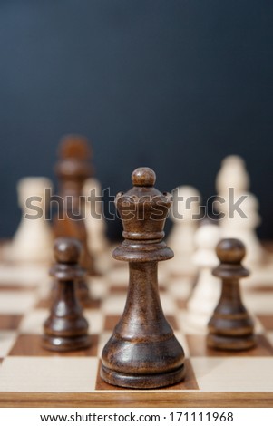 Still life close up detail view of a queen chess dark wooden piece on a chess board while a strategic game is being played. Interior professional strategy game playing.