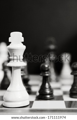 Black and white still life close up detail view of a king chess wooden piece on a chess board while a strategic game is being played. Professional game playing.