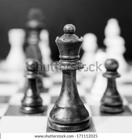 Black and white still life close up detail view of a queen chess dark wooden piece on a chess board while a strategic game is being played. Interior professional strategy game playing.