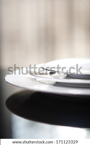 Close up still life detail view of a serving set of plates for one on a luxury reflective diner table in a quality home with smart curtains. Home interior detail view.