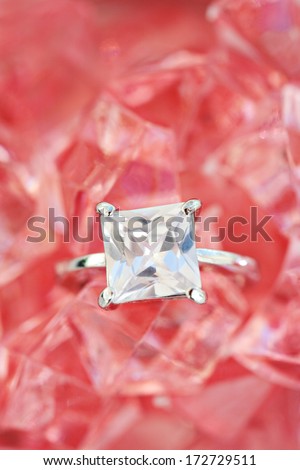 Close up detail view of a fine quality luxurious engagement ring on a pink rose minerals stone bed background. Diamond stone on white gold ring jewel and fashion accessory.
