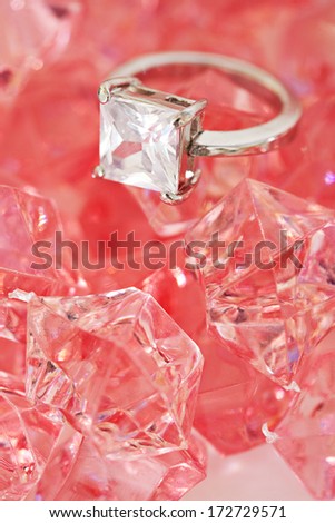 Close up detail view of a fine quality luxurious engagement ring on a pink rose minerals stone bed background. Diamond stone on white gold ring jewel and fashion accessory.