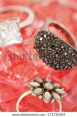 Close up detail view of fine quality luxury precious stones rings laying together on a pink rose stone minerals bed background. Diamond and stones white gold rings, fashion jewelery.