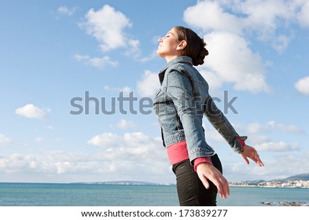 Side portrait view of a beautiful young woman on holiday by the sea, breathing fresh air on the coast against an intense blue sky during a sunny day. Outdoors lifestyle healthy beauty.