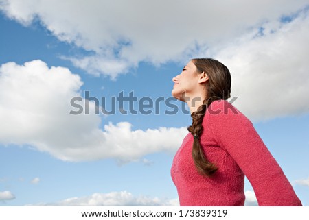 Close up profile portrait of an attractive young woman looking up against a sunny blue sky while on vacation, smiling and enjoying breathing fresh air. Outdoors lifestyle.