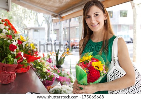 Portrait of an attractive young florist store customer client woman buying a bouquet of fresh flowers and smiling in a flower market stall store. Outdoors business shopping.