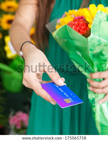 Close up detail view of a woman customer offering her credit card for payment and holding it in her hand while purchasing a colorful bouquet of flowers in a market stall florist shop, outdoors.
