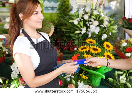 Side portrait view of an attractive shop attentant and business owner woman taking a customer credit card payment at a small florist business store outdoors. Outdoors shopping lifestyle.