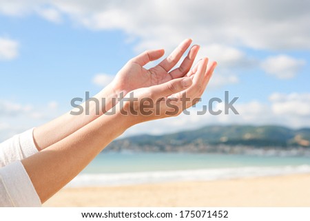 Close up profile view of a young woman arms and hands held together up against a sunny blue sky, holding an imaginary object during a sunny day on holiday. Outdoors lifestyle gesture.