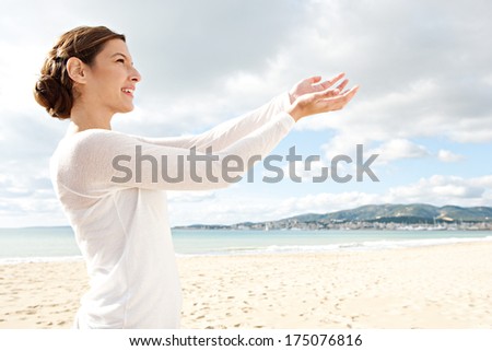 Close up profile portrait of a beautiful young woman on a white sand beach with her arms up extended in front of her holding an imaginary object in her hands. Outdoors lifestyle gesture.