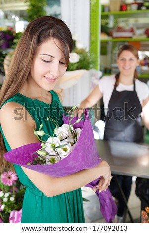 Lifestyle portrait of an attractive woman customer buying and holding a bouquet of fresh flowers in a florist market stall store shop, smiling. Outdoors small business.