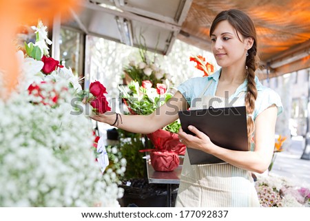 Close up portrait of a professional woman florist business owner checking the stock and inventory in her flower store holding a clipboard. Running a flower market stall, outdoors.