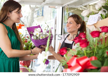Portrait of an attractive and smiling woman customer client buying a bouquet of white fresh flowers from a fresh flower market stall store and young shop attendant. Outdoors business shopping.