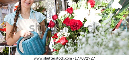 Panoramic view of a smiling florist shop assistant small business owner watering the plants and flowers in her store while smiling joyfully, Outdoors professional woman.