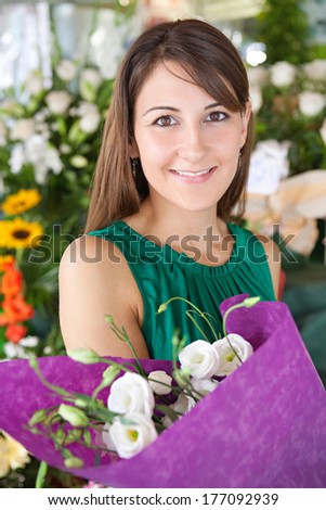 Close up portrait of an attractive young customer woman buying and holding a bouquet of fresh flowers while visiting a florist market stall in a city street. Outdoors lifestyle shopping.