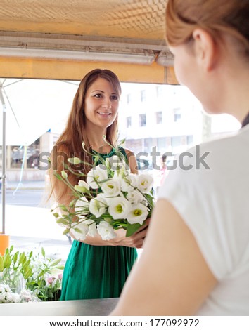 Portrait of an attractive florist store customer client woman buying a bouquet of fresh flowers and smiling at the store assistant in a flower market stall store. Outdoors business shopping.