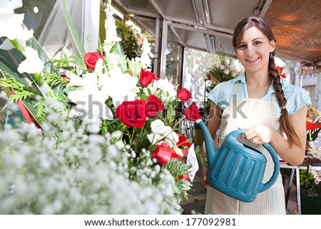 Portrait of an attractive florist shop assistant small business owner watering the plants and flowers in her store while smiling joyfully, Outdoors professional woman.