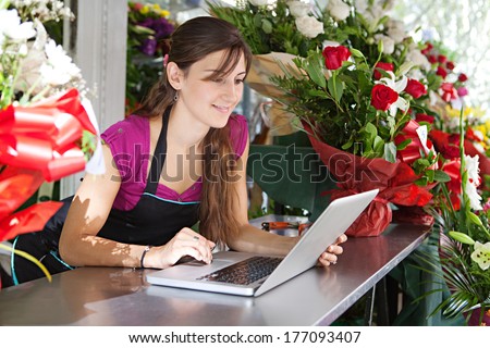 Portrait of an attractive florist business woman owner sitting at a flower shop counter using a laptop computer to place a stock order on line. Small business technology.