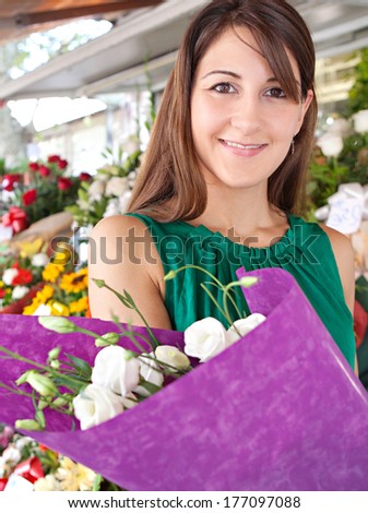 Close up portrait of an attractive young customer woman buying a bouquet of fresh flowers while visiting a florist market stall in a city street during a sunny day. Outdoors lifestyle shopping.