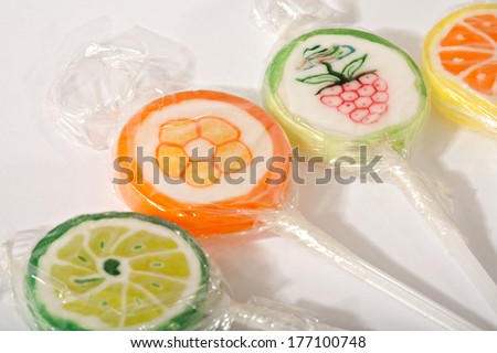 Still life detail view of various candy sweets with different fruit flavors wrapped in clear plastic laying together on a white background. Colorful sweet tooth sugar sticks.