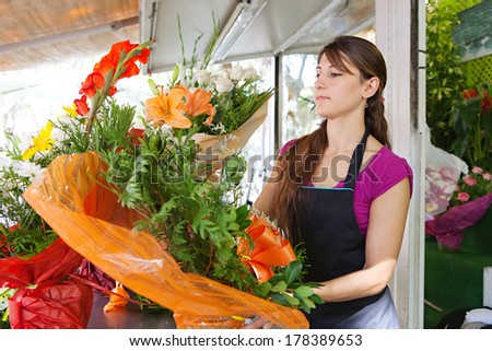Side portrait of an attractive florist business woman owner at a flower shop market working and making a new floral arrangement during a sunny day. Small business owner.