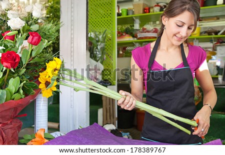 Portrait of a smiling florist business woman owner working at her flower store counter preparing an new floral arrangement cutting the stems of yellow sunflowers. Small business.