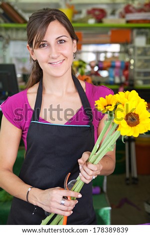 Portrait of a smiling florist business woman owner working at her flower store counter preparing an new floral arrangement holding yellow sunflowers. Small business owner.