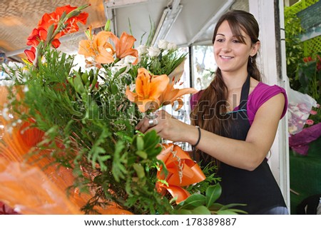 Portrait of an attractive florist business woman owner at a flower shop market working and making a new floral arrangement during a sunny day, smiling. Small business owner.