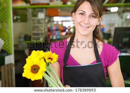 Portrait of a smiling florist business woman owner working at her flower store counter preparing an new floral arrangement holding yellow sunflowers. Small business owner.
